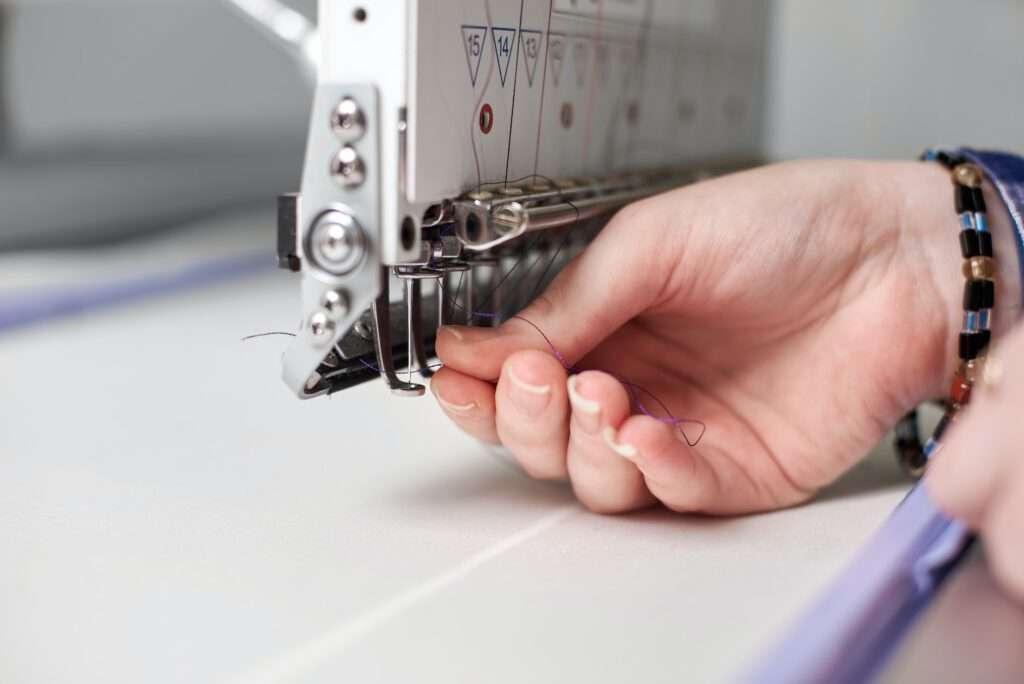 Nahaufnahme von Frauenhänden, die Faden in eine moderne Stickmaschine auf weißem Untergrund füllen copy space background.